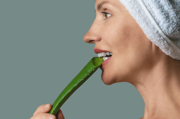 Side view happy woman, biting aloe vera leaf with white teeth on gray. Anti-aging care concept.