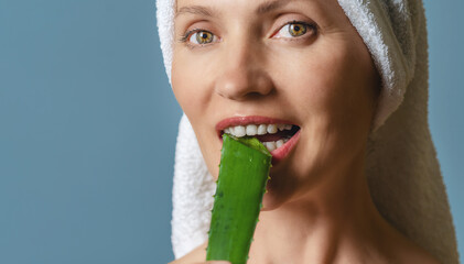 Portrait happy woman, biting aloe vera leaf with white teeth on blue. Anti-aging care concept.