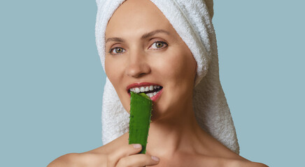 Portrait happy woman, biting aloe vera leaf with white teeth on soft blue. Anti-aging care concept.