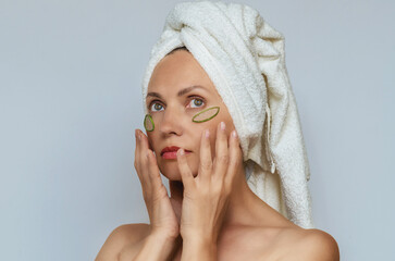 Dreamy woman in towel with aloe vera patches under eyes, hands near face. Skin hydration restoration