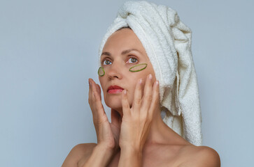 Dreamy woman in towel with aloe vera patches under eyes, hands near face. Skin hydration restoration