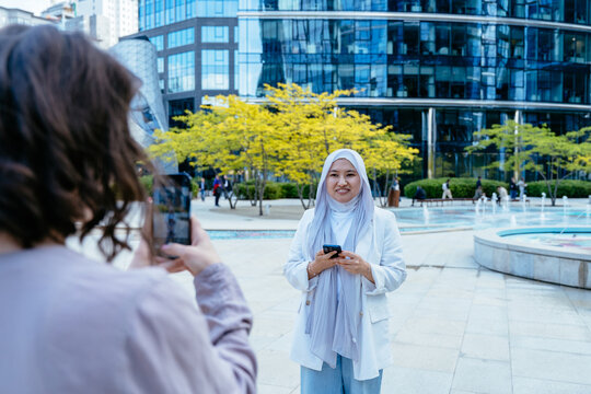Woman posing for smartphone photo near fountain in city