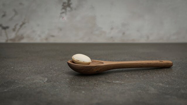An almond bean placed on a wooden spoon over a black stone countertop in a culinary area - Powered by Adobe