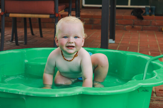 Baby boy playing in green plastic shell pool in summer