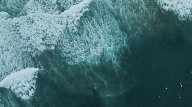 Aerial view of the ocean's turquoise water crashing into foamy white waves with surfers bobbing in the sea, San Diego, California, United States.
