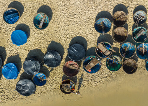 Aerial view of coracle boats with vibrant blue and black covers resting on the sandy beach, casting deep shadows, Vietnam, Vietnam.