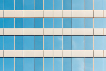 Reflective facade: A modern building's glass exterior mirrors the sky, creating a symmetrical pattern of blue and white. Architectural elegance.