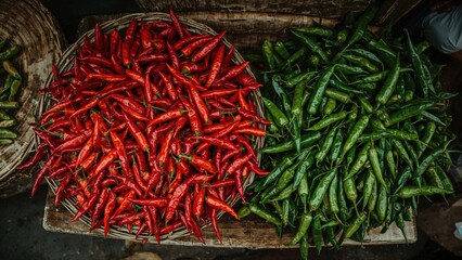 Bird's-eye view of a heap of freshly picked red and green chili peppers in a basket at a market stall.
