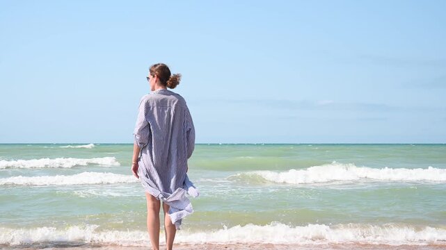Lonely woman on sandy seashore, ocean, video. Beautiful landscape with sea view, waves and blue sky.