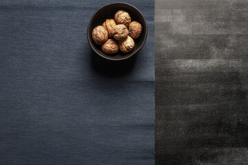 Black bowl with walnuts and blue table cloth on black chalkboard background. Flat lay. Top view.