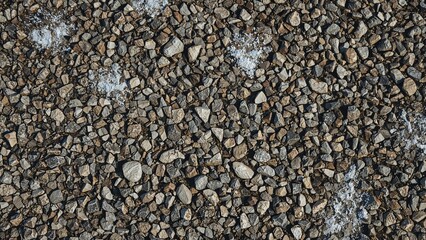 Sharp close-up of a pebble road with scattered snowflakes, showing a textured and raw surface. Ideal for backgrounds, design work, and rustic-inspired compositions.