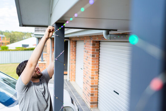 Man stringing up smart fairy lights at front of house for christmas