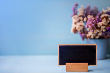 
wooden blackboard on table with dry flower pot over blue wall background.
