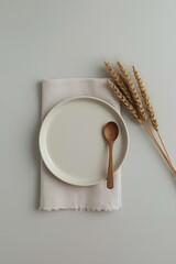A neutral-toned ceramic plate, light beige fabric napkin, wooden spoon, dried wheat stalks, and soft gray background create a minimalist, earthy, and elegant aesthetic.