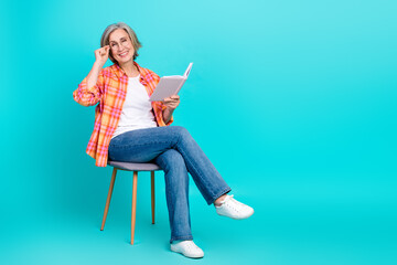 Charming elderly woman wearing stylish attire and reading a book while seated against a vibrant...