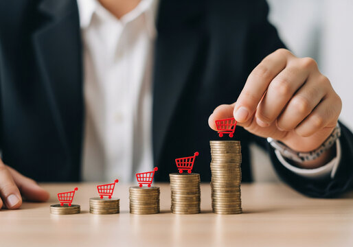 A professional businessman in a black suit is arranging small red shopping cart icons on top of stacks of gold coins, concept growth in sales or investments.