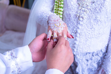 The hand of an Asian man  is attaching a wedding ring to the hand of an Asian woman at a wedding...