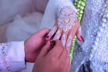 The hand of an Asian man  is attaching a wedding ring to the hand of an Asian woman at a wedding...