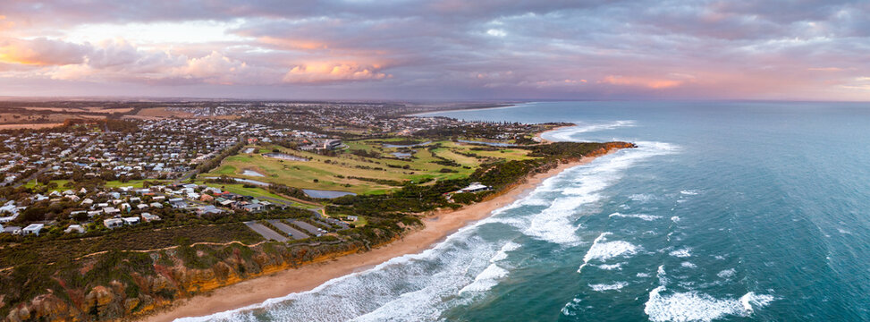 Aerial panorama of a colourful sky over a coastal golf course and waves on the beach below