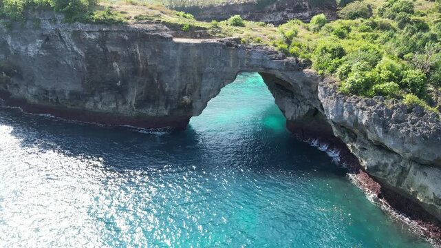 Epic drone shot of the massive Arch Ole Oli, a stunning natural rock formation at Broken Bay Cliff, Nusa Penida, Bali.