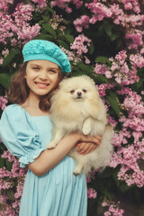 Smiling girl holding Pomeranian dog in blooming garden