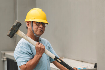 Serious-looking Southeast Asian demolition crewman in safety gear rests heavy sledgehammer on...