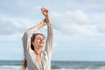 young carefree woman in casual outfit standing at the beach,closed eyes,arms outstretched,relaxing,feeling breeze and freedom,happy caucasian female tourist in seashore on summer vacation