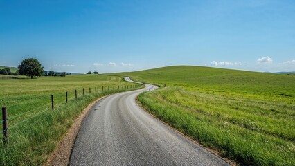 Obraz premium Winding asphalt trail stretches over lush grasslands with a clear sky above.