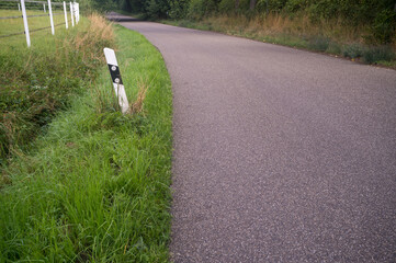 Winding country road leading into lush green forest with reflectors and white fence