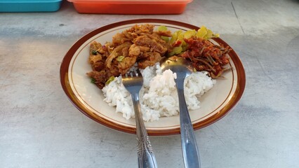 A plate of traditional breakfast featuring steamed rice served with colorful cap cay (mixed stir-fried vegetables), sautéed bitter melon, and spicy anchovy chili paste. This flavorful combination