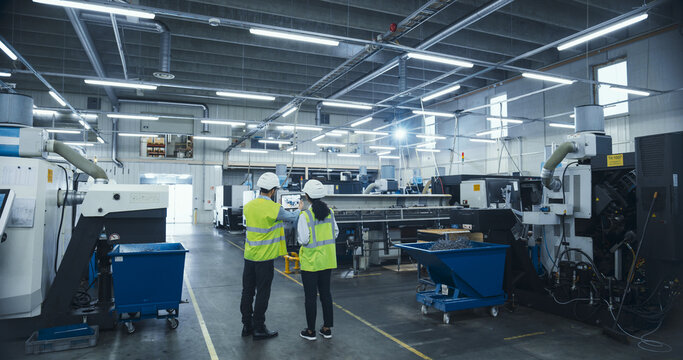 Manufacturing Process Manager and Equipment Supervisor Having a Meeting on Factory Floor, Discussing Production Technology, Strategic Business Partnerships, Metal Component Delivery Techniques