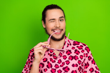 Fashionable young man winking in bright pink leopard print shirt against green studio backdrop