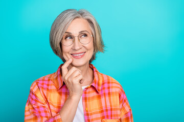 Smiling mature woman with gray hair in casual plaid shirt posing against bright turquoise backdrop with thoughtful expression