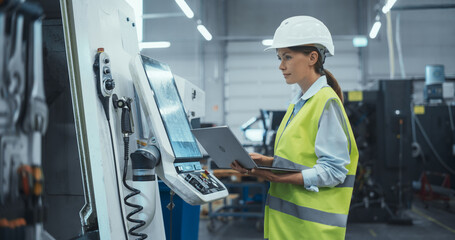 Female Machinery Technician Using Laptop Computer and Programming a CNC Machine at an Advanced...