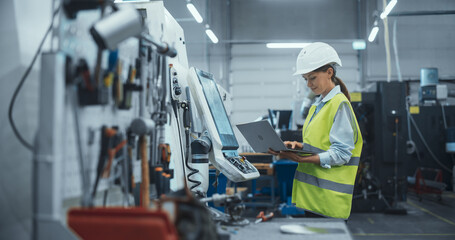 Female Machinery Technician Using Laptop Computer and Programming a CNC Machine at an Advanced...