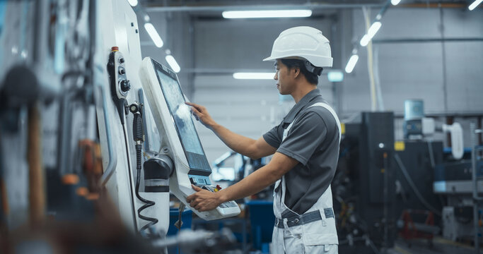 Asian Male Engineer in a White Hard Hat Operating a CNC Milling Machine in a Modern Factory. Young Technician Inserting Parameters on a Touch Screen Display, Automating Production Line - Powered by Adobe