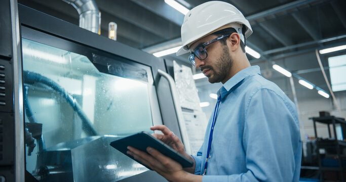 Industrial Engineer at Work. Multiethnic Male Using Tablet Computer to Update Settings, Downloading New Production Instructions for the CNC Machine in a High Tech Metal Factory