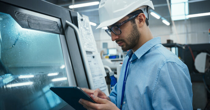 Industrial Engineer at Work. Multiethnic Male Using Tablet Computer to Update Settings, Downloading New Production Instructions for the CNC Machine in a High Tech Metal Factory