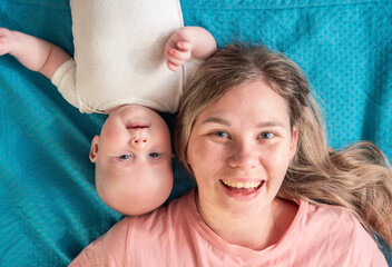 Mother and baby share a joyful moment lying on a blue blanket in a cozy indoor setting