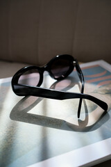 Stylish black sunglasses resting on white table surface with shadow cast by natural sunlight, creating elegant minimalist composition for fashion and lifestyle concepts.