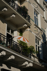 Historic Hamburg apartment building facade with ornate architectural details, decorative balconies, wrought iron railings, green plants, and orange umbrella in charming German residential district.