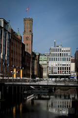 Historic Hamburg city center with iconic brick clock tower and modern buildings reflected in canal water. Traditional German architecture mixed with contemporary urban development along waterfront.