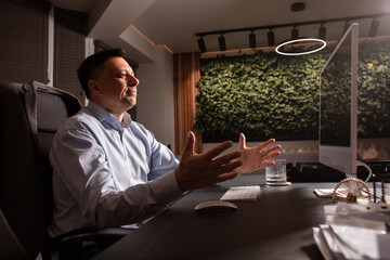 Upset businessman raises his hands in frustration while working at a cluttered office desk. Symbol...