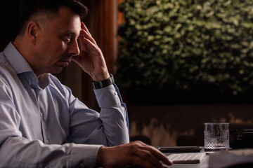 Focused man in a light shirt holds smartphone while working at a stylish evening office. Modern...