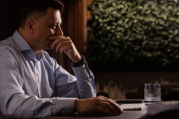 Focused man in a light shirt holds smartphone while working at a stylish evening office. Modern...