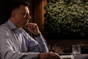 Focused man in a light shirt holds smartphone while working at a stylish evening office. Modern...