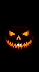 Fototapeta premium Glowing jack-o’-lantern with sharp teeth and sinister eyes carved into a pumpkin, grinning in total darkness perfectly eerie Halloween atmosphere