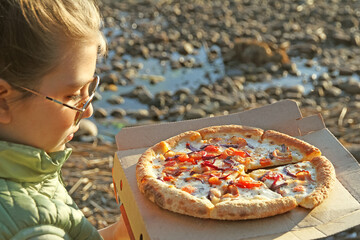 Child holding pizza paper box on beach in sunset light