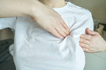 Female adjusting white t shirt fit on chest with hands indoors.