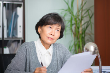 A mature Asian woman evaluates performance reviews for her department, looking for trends and gaps while offering constructive, thoughtful feedback in personalized evaluations